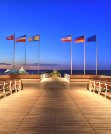 Die Seebrücke Boltenhagen ragt in die Ostsee. Beleuchtet bei Nacht. Fahnen wehen am Ende.