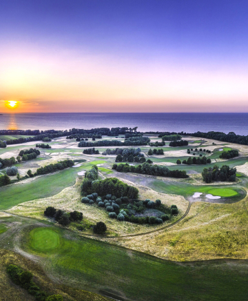 Ein Golfplatz aus der Luft. Im Hintergrund die Ostsee bei Sonnenuntergang.