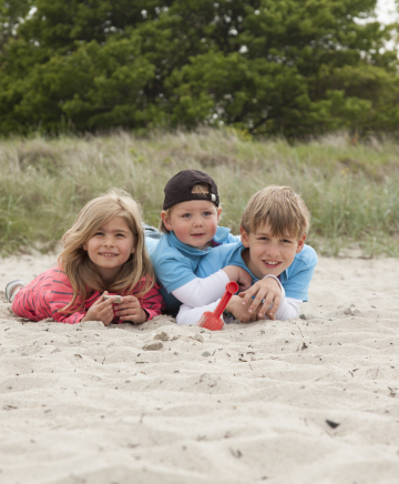 Drei Kinder liegen am Strand.