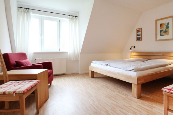Blick in das Schlafzimmer mit einem Doppelbett, Stuhl, Tischchen und Sessel
