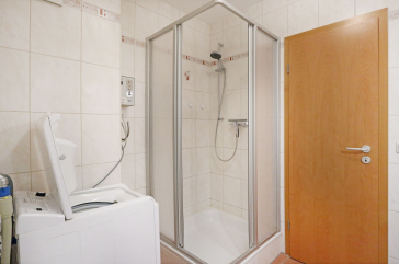 Blick in das Duschbad mit Waschmaschine, Waschbecken und Spiegel
