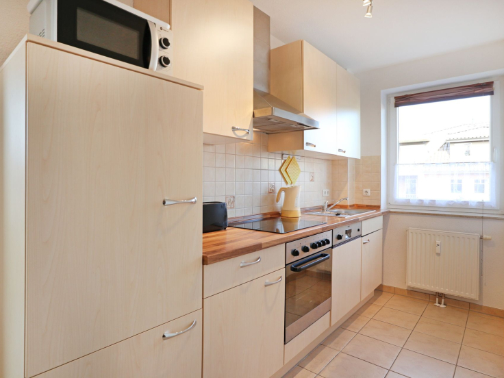 Blick auf die offene Küchenzeile mit Kühlschrank, Mikrolwelle, Backofen, Ceranfeld und Geschirrspüler