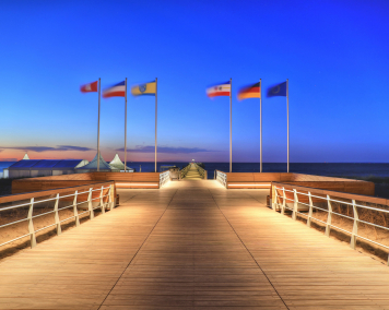 Die Seebrücke Boltenhagen ragt in die Ostsee. Beleuchtet bei Nacht. Fahnen wehen am Ende.