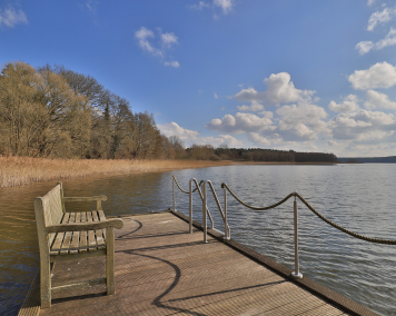 Eine Bank auf einem Steg. Der Steg liegt in einem See.
