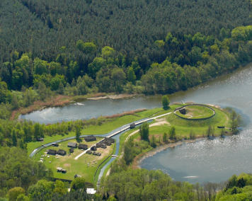 Ein See mit einer Halbinsel mit Gebäuden drauf umgeben vom Wald