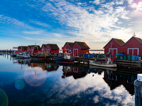 Boote sind vor kleinen Häusern angetäut. Spiegelglatte Wasseroberfläche.