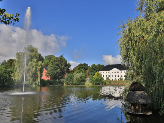 Blick auf das Hauptgebäude des Schlossgut Gross Schwansse mit Teich und Brasserie