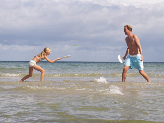 Ein Mädchen und ein Mann spielen Badminton im flachen Meereswasser.