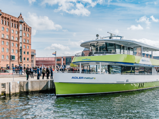 Grünes Schiff im Hafenwasser, im Hintergrund ein Backsteingebäude